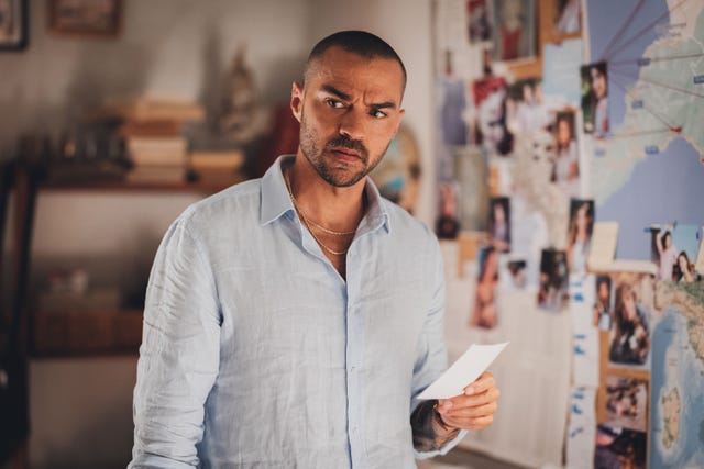 Person showing a piece of paper in front of a wall covered with photographs and a map