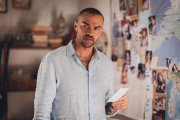 Person showing a piece of paper in front of a wall covered with photographs and a map