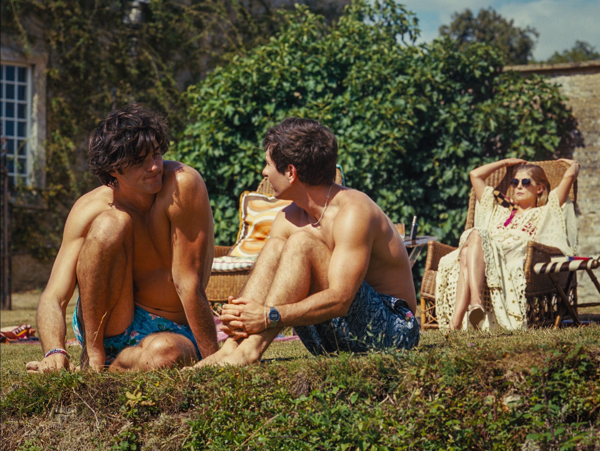 a couple of men sitting on the grass looking at a man