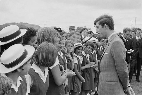 prince charles stands in front of and talks to a group of schoolgirls wearing uniforms, charles is wearing a suit