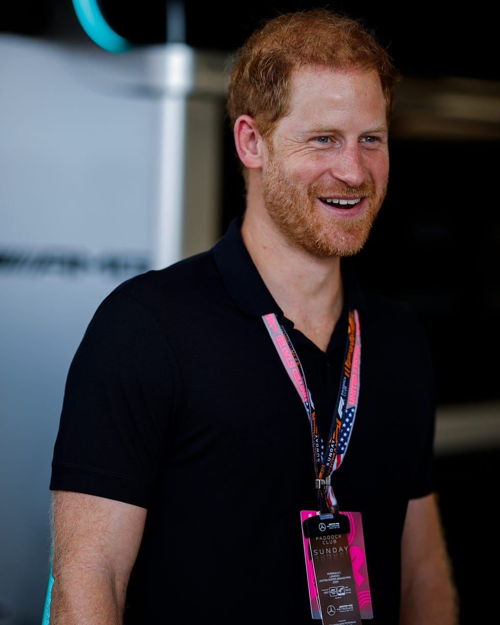 Prince Harry, Duke of Sussex on October 22, 2023 prince harry smiles and looks right, he wears a black polo shirt and two lanyards around his neck with cards on the bottom