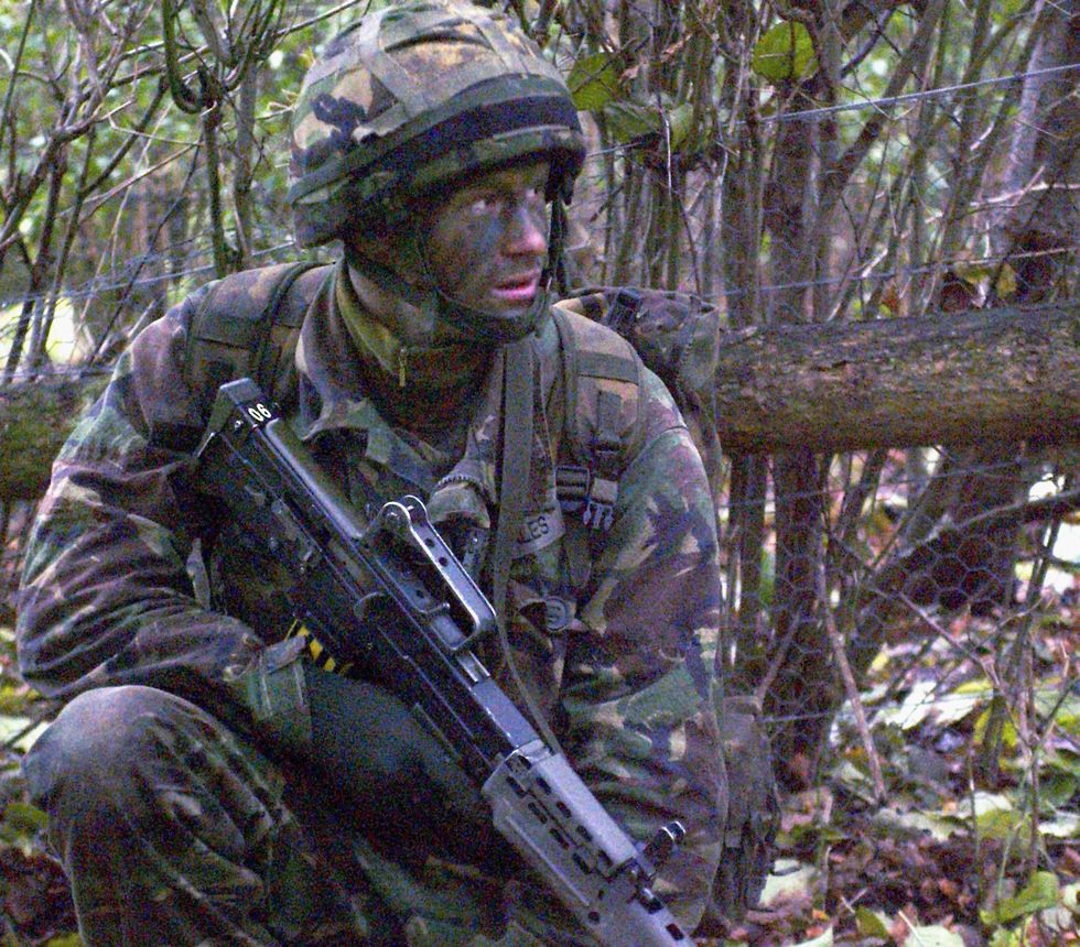 prince harry wearing camouflage and face paint and holding a gun during military training