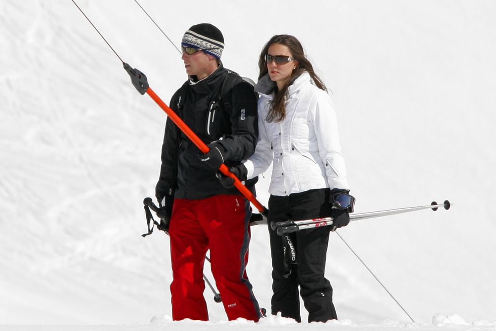 prince william and kate middleton hold onto a red tbar ski lift, both wear snow pants and coats with sunglasses and hold ski poles