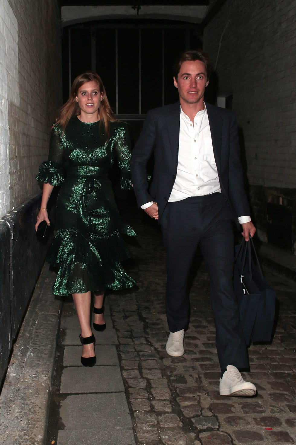 Princess Beatrice walking through the street in a glamorous green dress holding hands with her smartly dressed fiance, Edo Mapelli Mozzi.