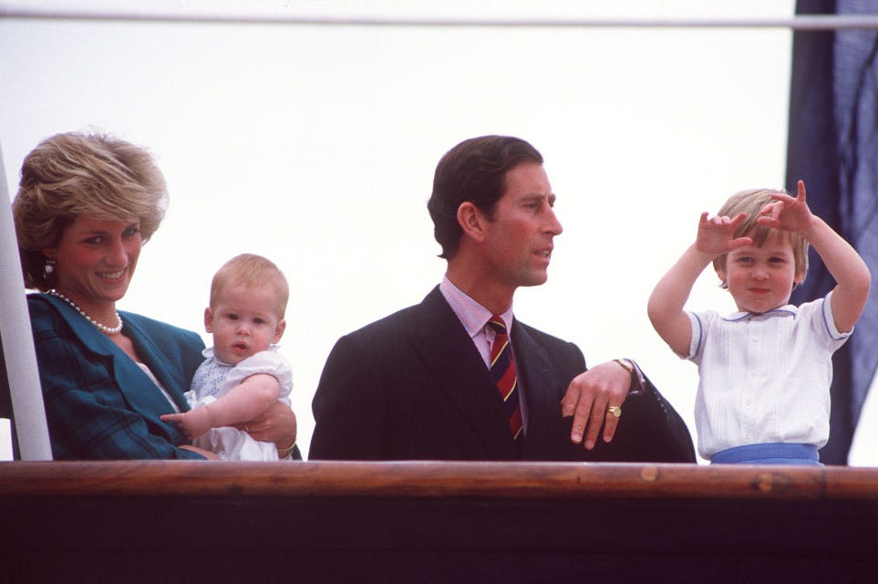 princess diana holds baby ﻿prince harry and stands next to then prince﻿ charles and prince william behind a wooden railing