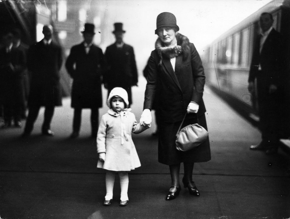 a young princess elizabeth, about three years old, holdsher grandmother's hand at the train station