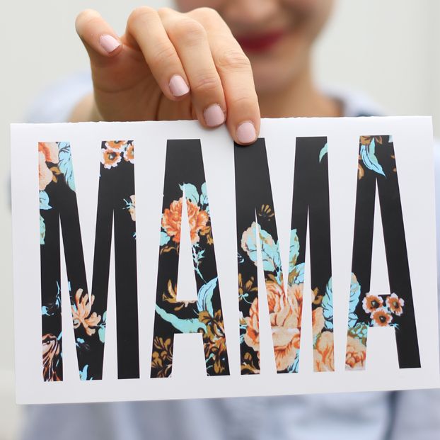 woman holding white card in front of her that says mama in black all caps with a peach and aqua floral pattern on the letters