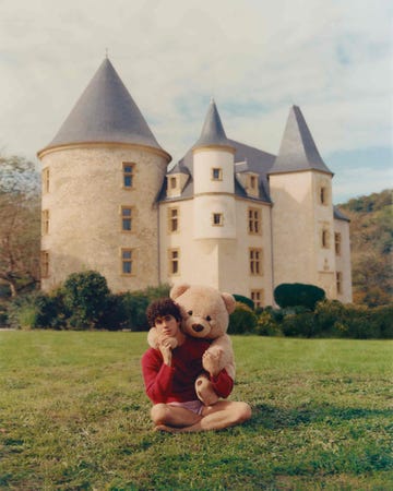 child sitting on grass holding a large teddy bear with a castle in the background