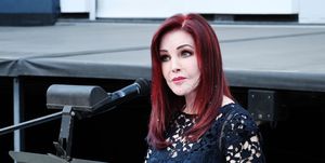 priscilla presley standing at a podium with a microphone and looking out toward an audience