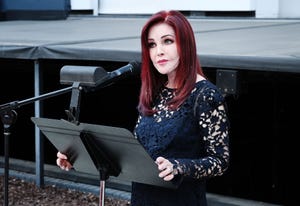 priscilla presley standing at a podium with a microphone and looking out toward an audience