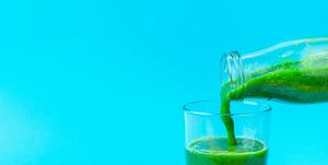 Process of Pouring from Bottle to Glass of Green Fresh Smoothie from Leafy Greens Vegetables Fruits. Apples Bananas Kiwi Zucchini Spinach on Light Blue Background. Healthy Lifestyle Detox Vitamins