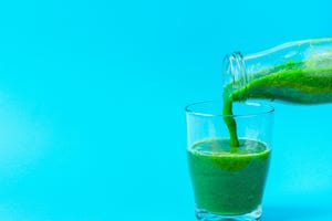 Process of Pouring from Bottle to Glass of Green Fresh Smoothie from Leafy Greens Vegetables Fruits. Apples Bananas Kiwi Zucchini Spinach on Light Blue Background. Healthy Lifestyle Detox Vitamins