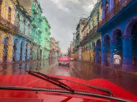 Een eenzame passant slentert door een regenbui in december in Havana De foto is genomen door de voorruit van een van de iconische autos uit jaren 1950 die in Cuba rondrijden De rechterruitenwisser werkte niet zodat de regen voor een impressionistisch effect zorgde