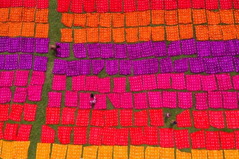 Een luchtfoto van kinderen die heldere kleurrijke batikdoeken neerleggen op een open veld nabij Dhaka in Bangladesh Ze schieten hun ouders die voor een batikfabriek werken vaak te hulp onder werktijd Oudere kinderen passen ook op de kleintjes wanneer hun ouders aan het werk zijn