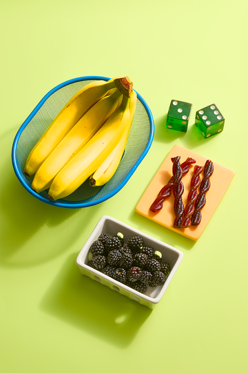bananas, blackberries and dried fruit snacks with green dice on a table