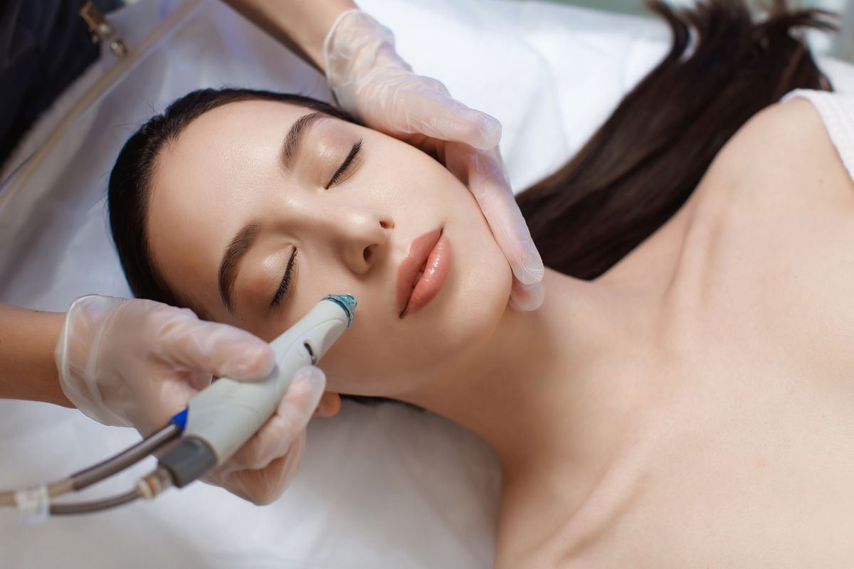 professional female cosmetologist doing hydrafacial procedure in cosmetology clinic
