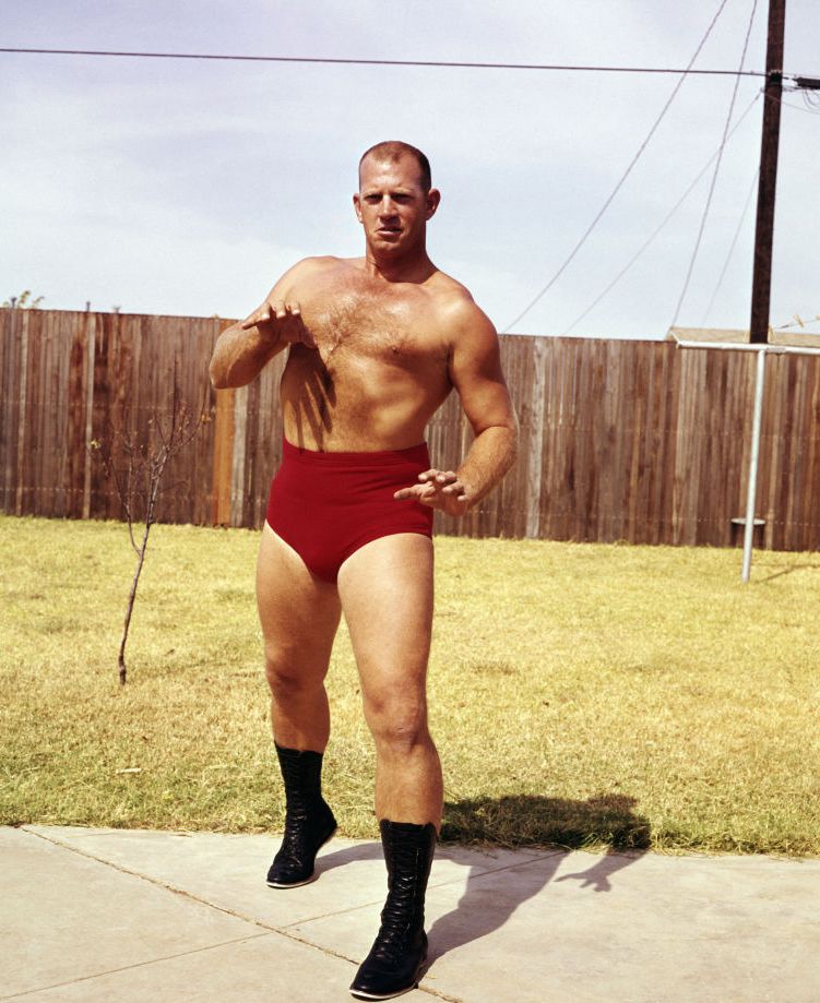 fritz von erich standing in a yard with a fence pretending to square up to an opponent in his wrestling attire