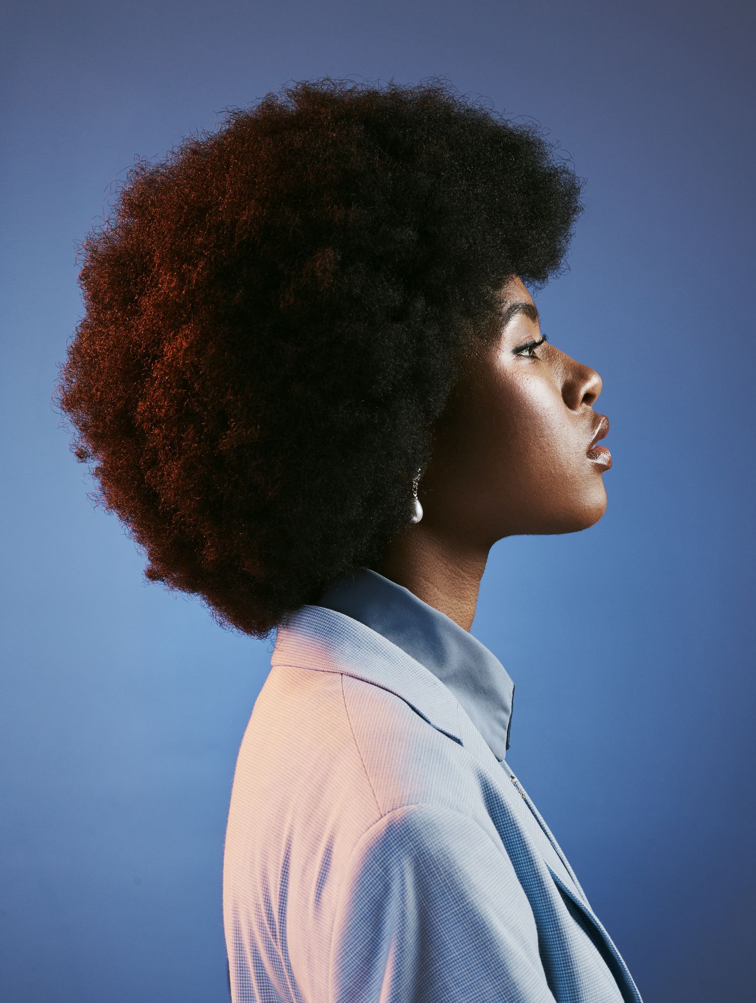 profile of fierce, afro and retro model with attitude, perfect skin and a cool, funky and trendy hairstyle. a powerful portrait of intense, proud and fashionable woman against blue studio background
