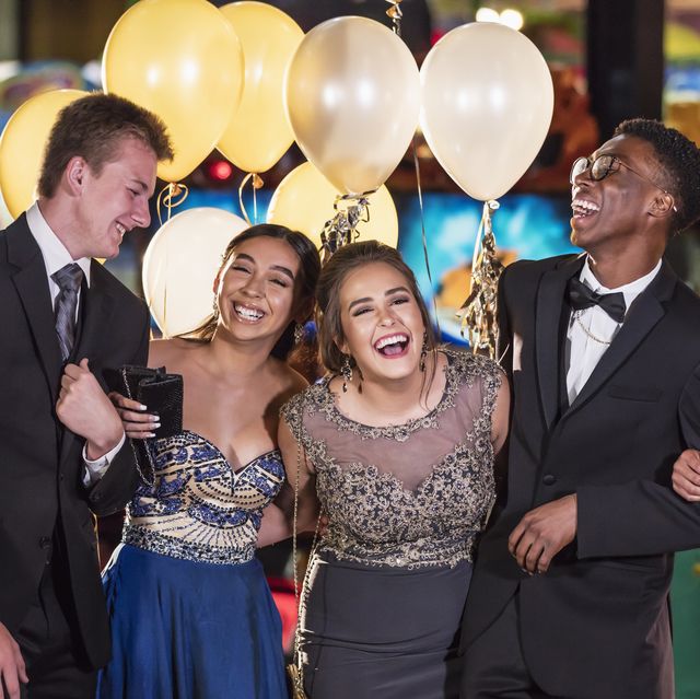 a multi ethnic group of six teenagers, three multi ethnic couples, having fun at their high school prom the two girls are wearing prom dresses and their dates are wearing a suit and tuxedo