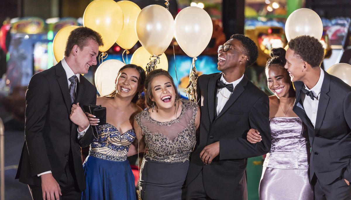 a multi ethnic group of six teenagers, three multi ethnic couples, having fun at their high school prom the two girls are wearing prom dresses and their dates are wearing a suit and tuxedo