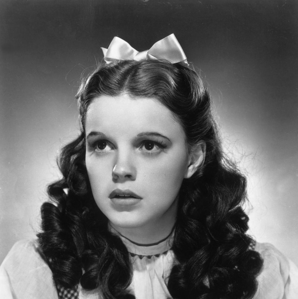 promotional studio portrait of american actor and singer judy garland wearing her costume as dorothy from director victor fleming's film the wizard of oz she wears a gingham bodice and a white puff sleeved blouse, with a satin ribbon in her hair