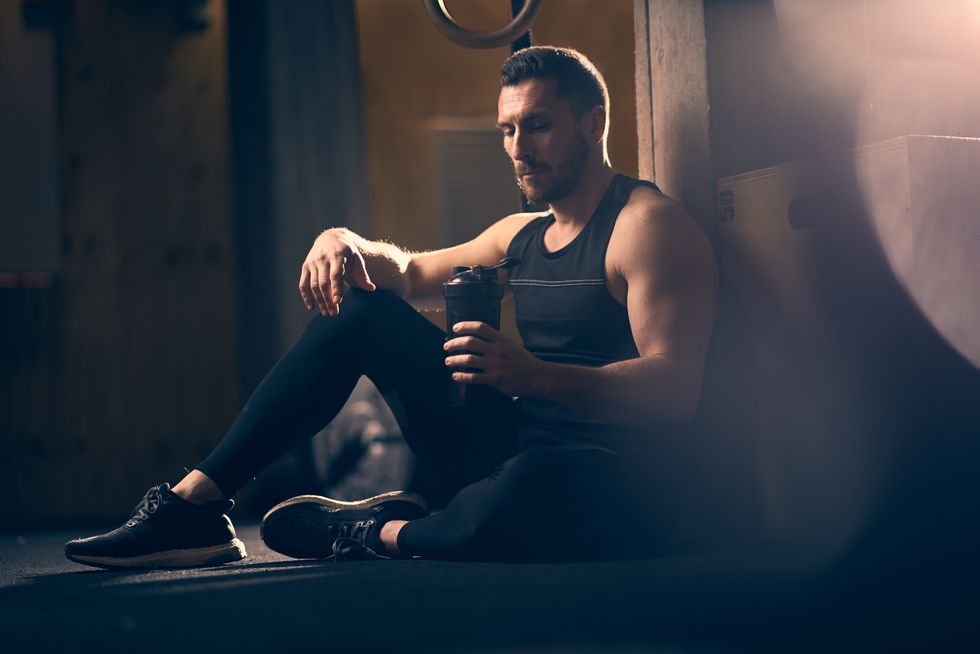 male athlete holding shaker bottle and resting after cross training class in the gym