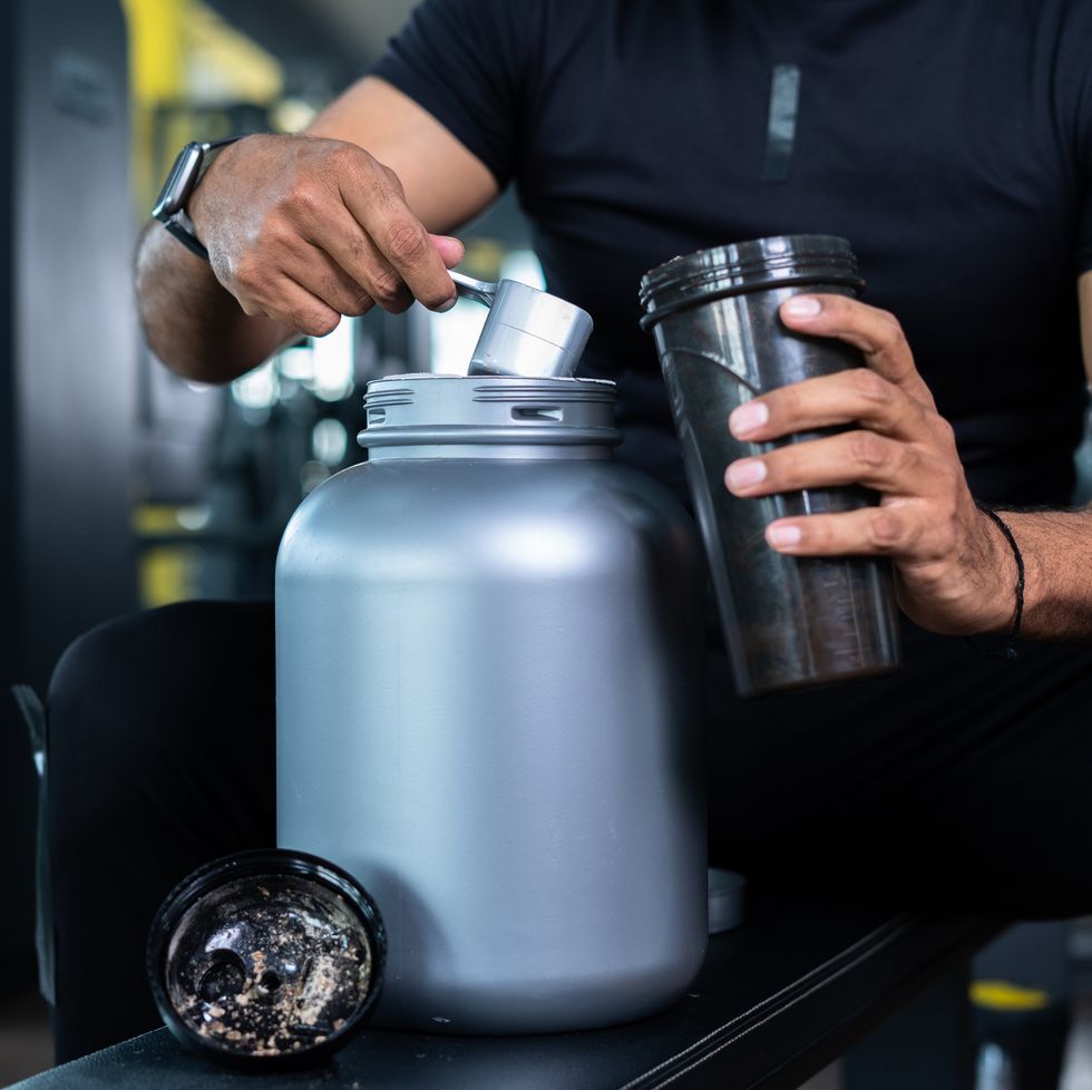 close up shot of bodybuilder hands taking protein powder and mixing with water on bottle by shaking at gym   concept of muscular gain, nutritional supplement and wellness