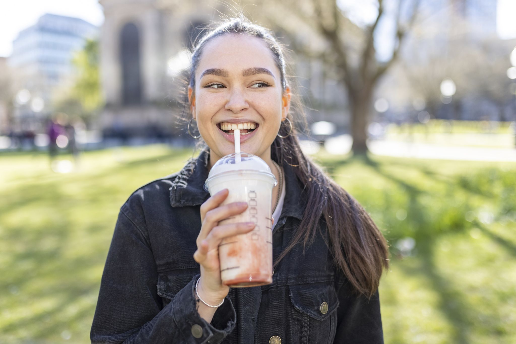 a woman drinking a smoothie in a park