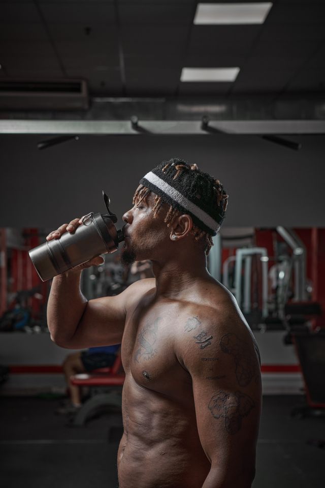 protein shake after workout and gym training african american man with naked torso drinking sport drink