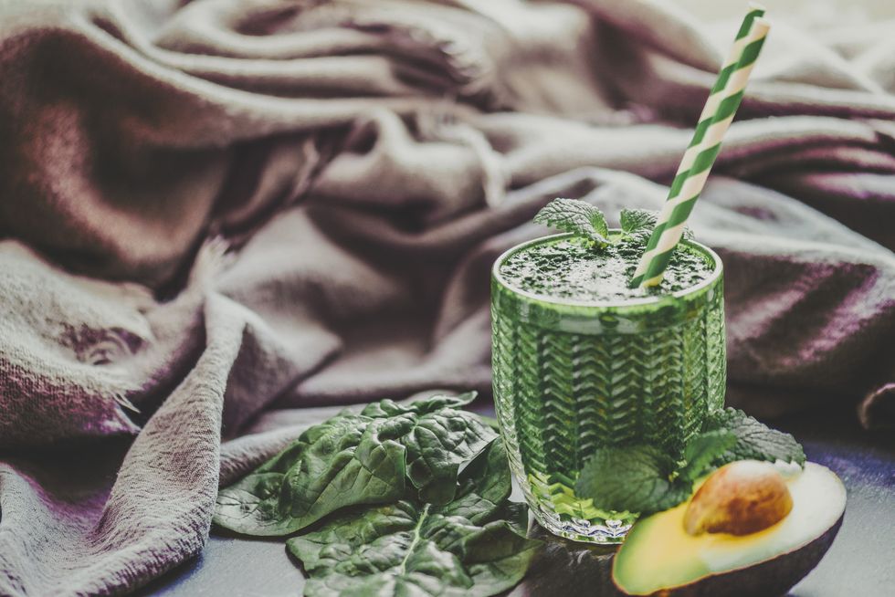 green smoothie and some ingredients such as vegetables, fruits and chlorella powder shot on a slate with a sustainable straw