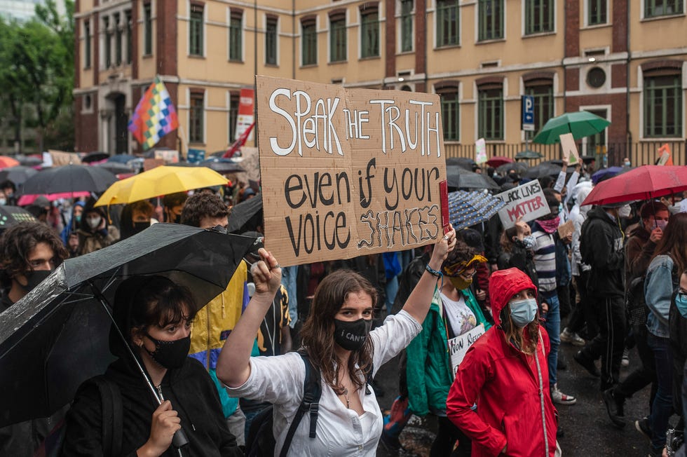woman holding up sign that reads 'speak the truth even if your voice shakes'