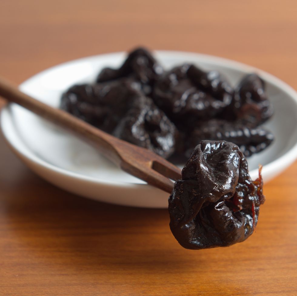 prunes in a white bowl with a wooden fork on a wooden table