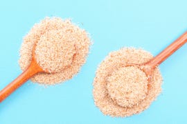 two wooden spoons of psyllium husk on a blue background top view, close up.