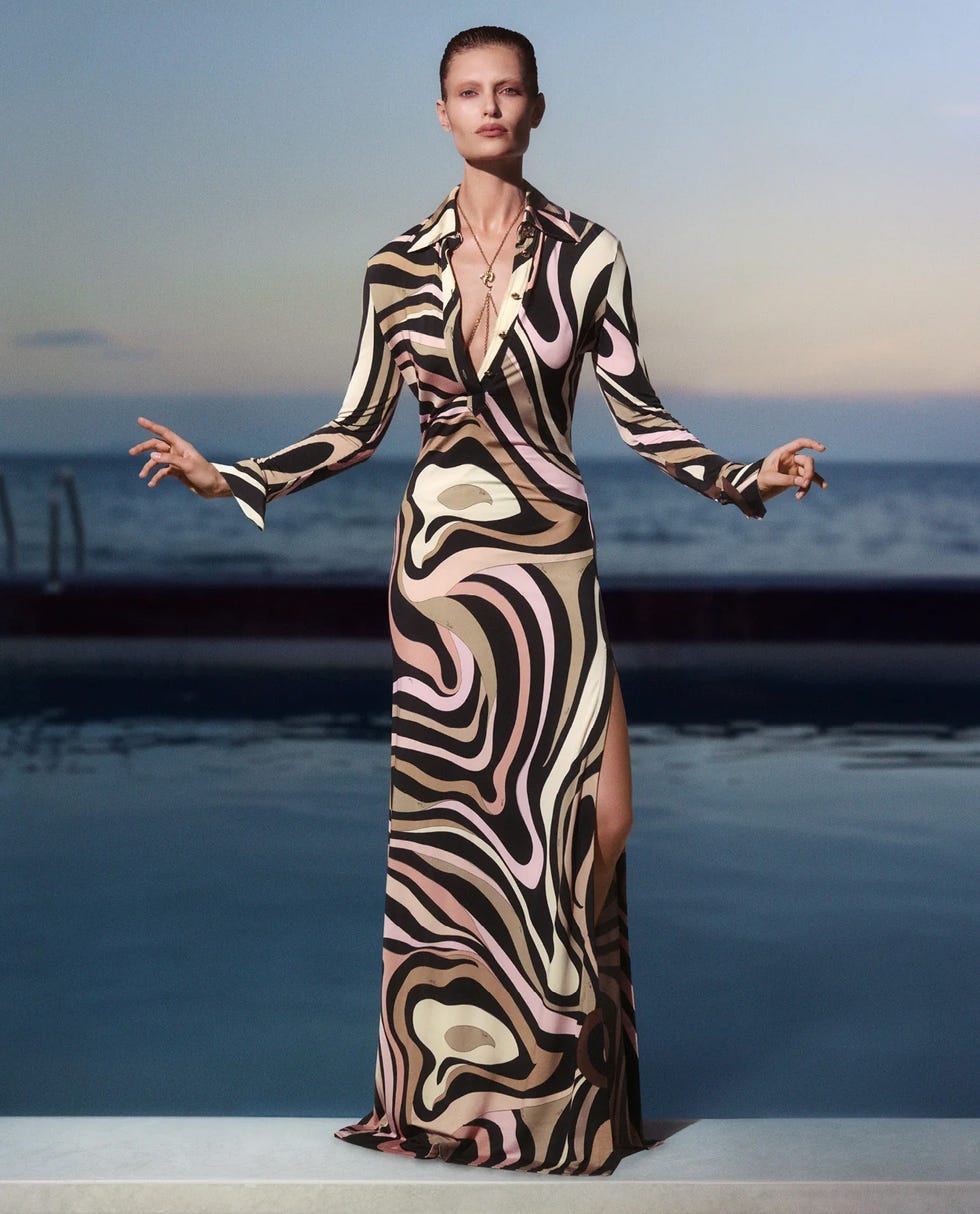 a figure wearing a patterned maxi dress stands near a pool at sunset