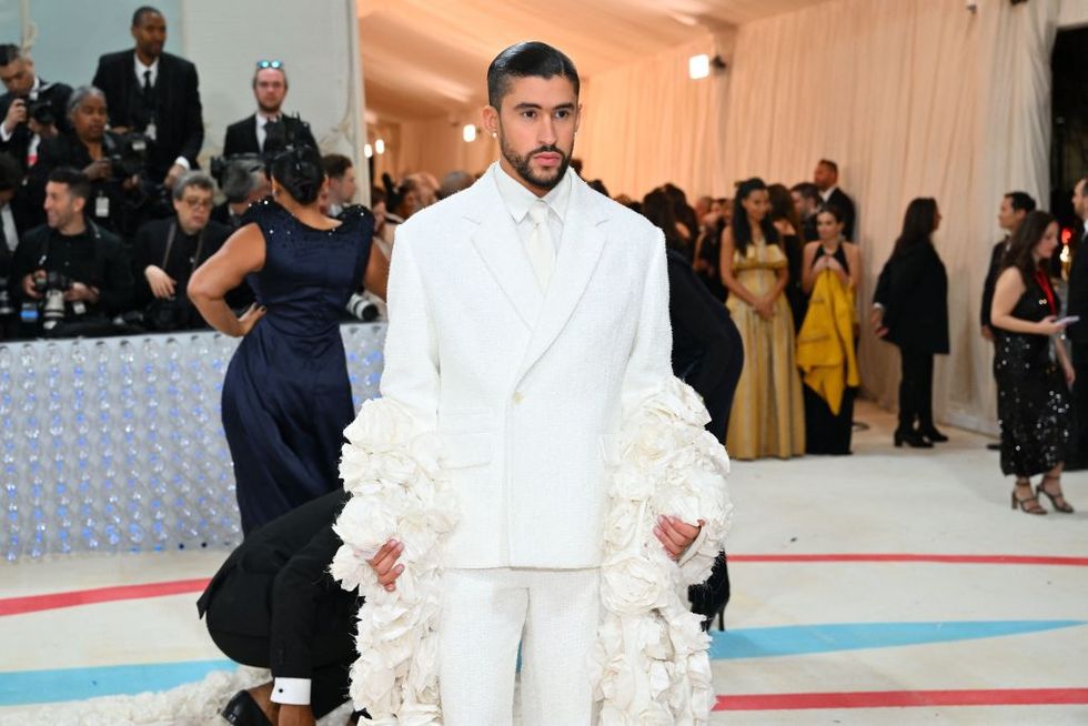 bad bunny wearing a white suit and tie with lage white frills on the sleeves