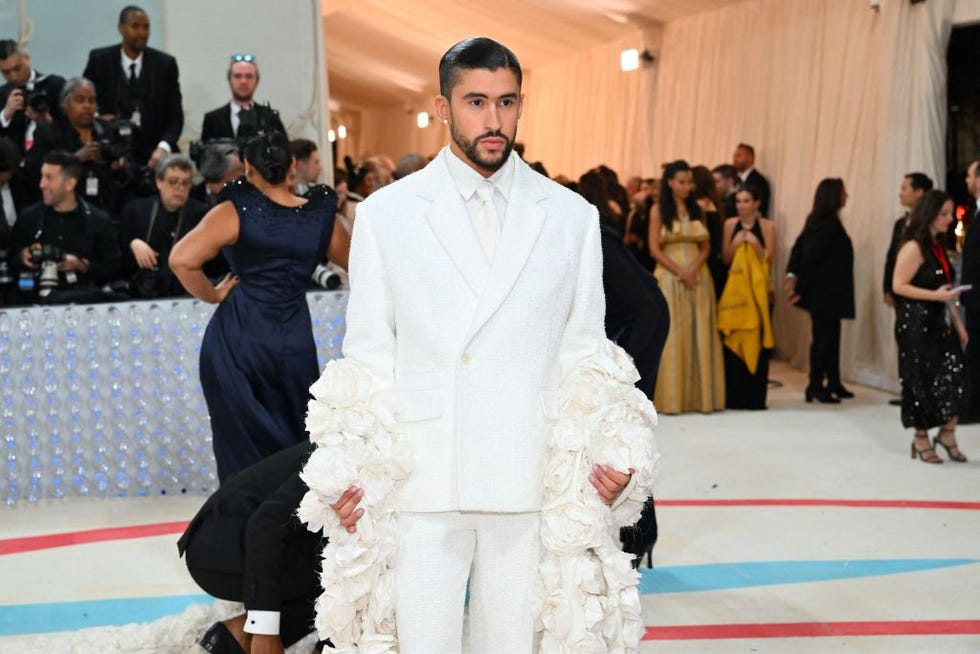 bad bunny wearing a white suit and tie with lage white frills on the sleeves