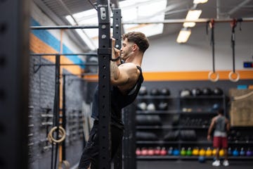side view of fit young man doing chin ups on a bar at fitness studio. male exercising in a cross training gym.