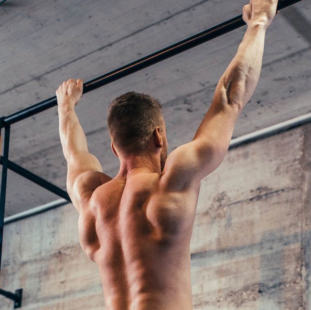 man hanging from a wall mounted pull up rack