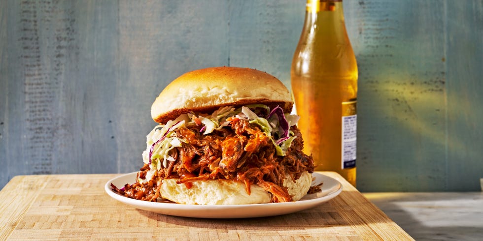pulled pork sandwich on a plate with a beer in the background
