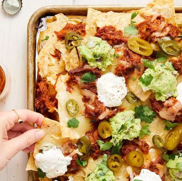 tortilla chips on a sheet pan topped with pulled pork, guacamole, sour cream, and jalapenos
