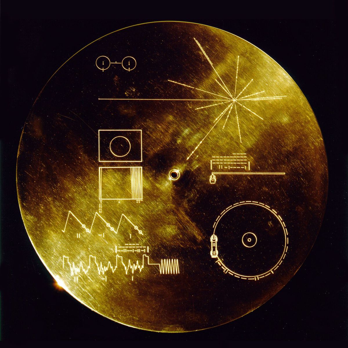 Deze beschermkap gemaakt van een goudaluminiumverbinding werd ontworpen om de Golden Records gouden grammofoonplaten op de sondes Voyager 1 en 2 te beschermen tegen het bombardement van micrometeorieten maar diende ook nog een andere doel hij gaf de eventuele vinders aanwijzingen voor het afspelen van de grammofoonplaat Het verklarende diagram staat zowel op de binnen als buitenkant van de beschermkap omdat het diagram op de buitenkant na verloop van tijd zou wegslijten