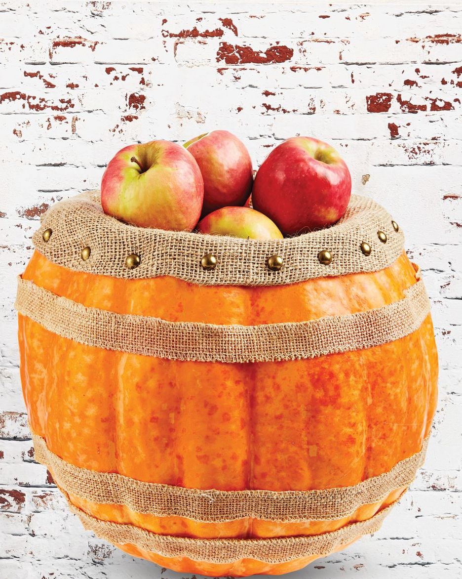 carved pumpkin decorated with burlap strips and nailhead trim to resemble a barrel, filled with apples