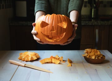 pumpkin carving, woman holding a carved smiley faced pumpkin over the table with a carving knife