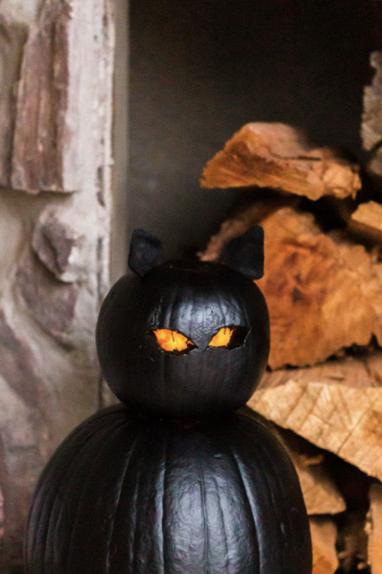 pumpkin carving ideas, two black pumpkins stacked on top of each other to look like a cat with carved out eyes