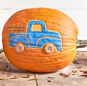 pumpkin carved and painted with blue pickup truck design appearing to haul a toy green trailer filled with mini pumpkins