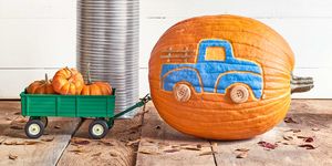 pumpkin carved and painted with blue pickup truck design appearing to haul a toy green trailer filled with mini pumpkins