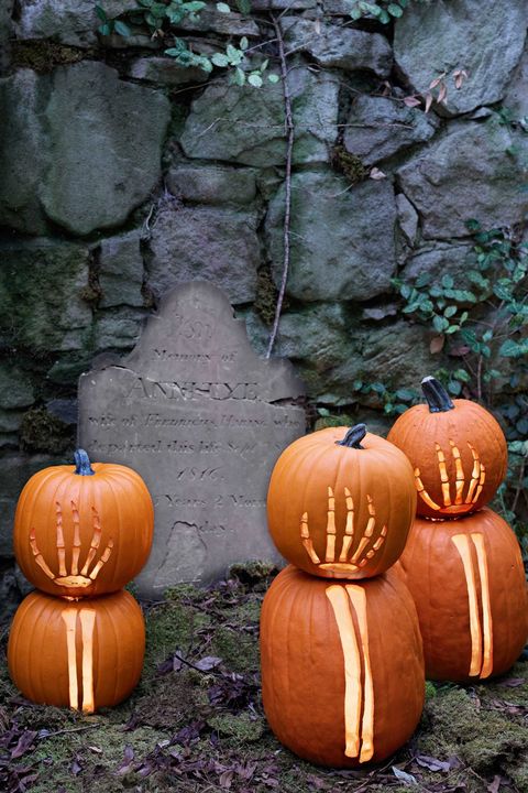 stacked pumpkins with hand and arm skeleton carvings in front of spooky cracked gravestone and old stone wall