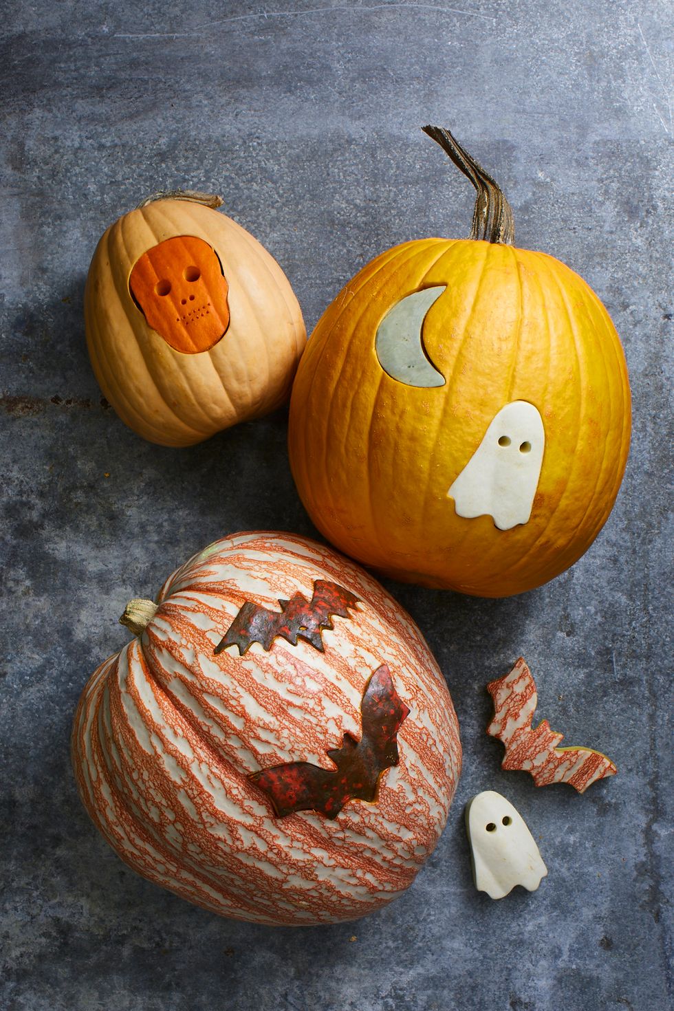 pumpkin carving ideas, three pumpkins with different shapes punched into them, like ghosts, bats and skeletons