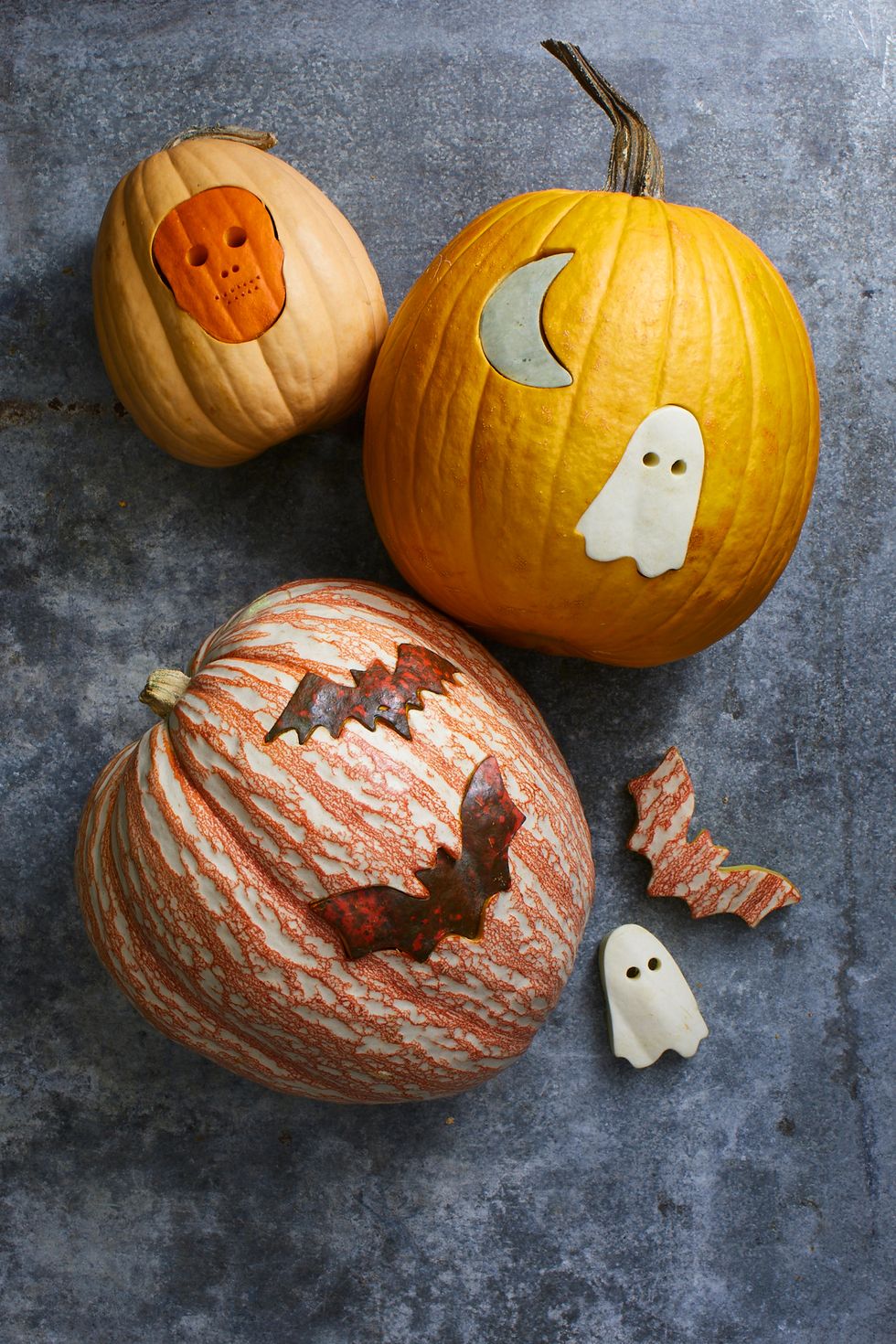 pumpkin carving ideas, three pumpkins with different shapes punched into them, like ghosts, bats and skeletons