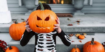 kid in skeleton costume holding up jack o lantern carved pumpkin